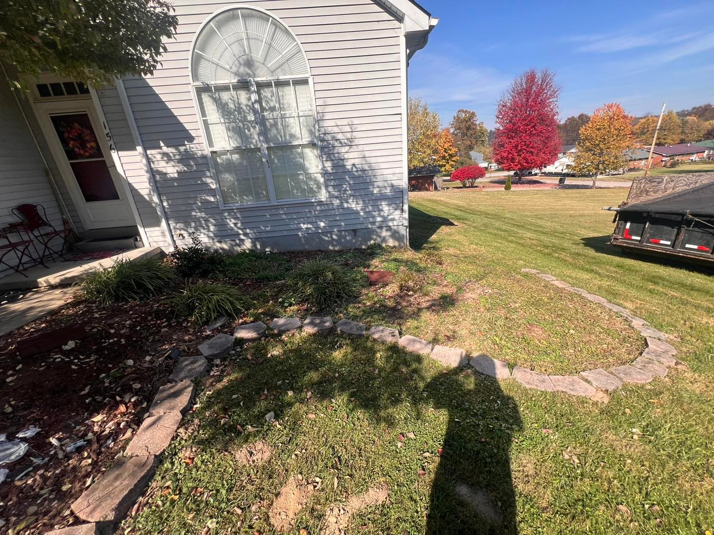 Landscaped yard featuring stone pathway, vibrant autumn trees, and a home with large window.