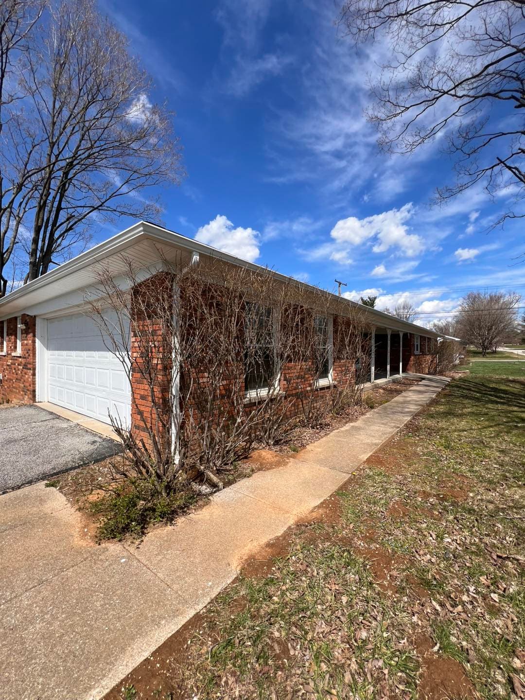 One-story brick house with garage, sidewalk, and clear blue sky in background.