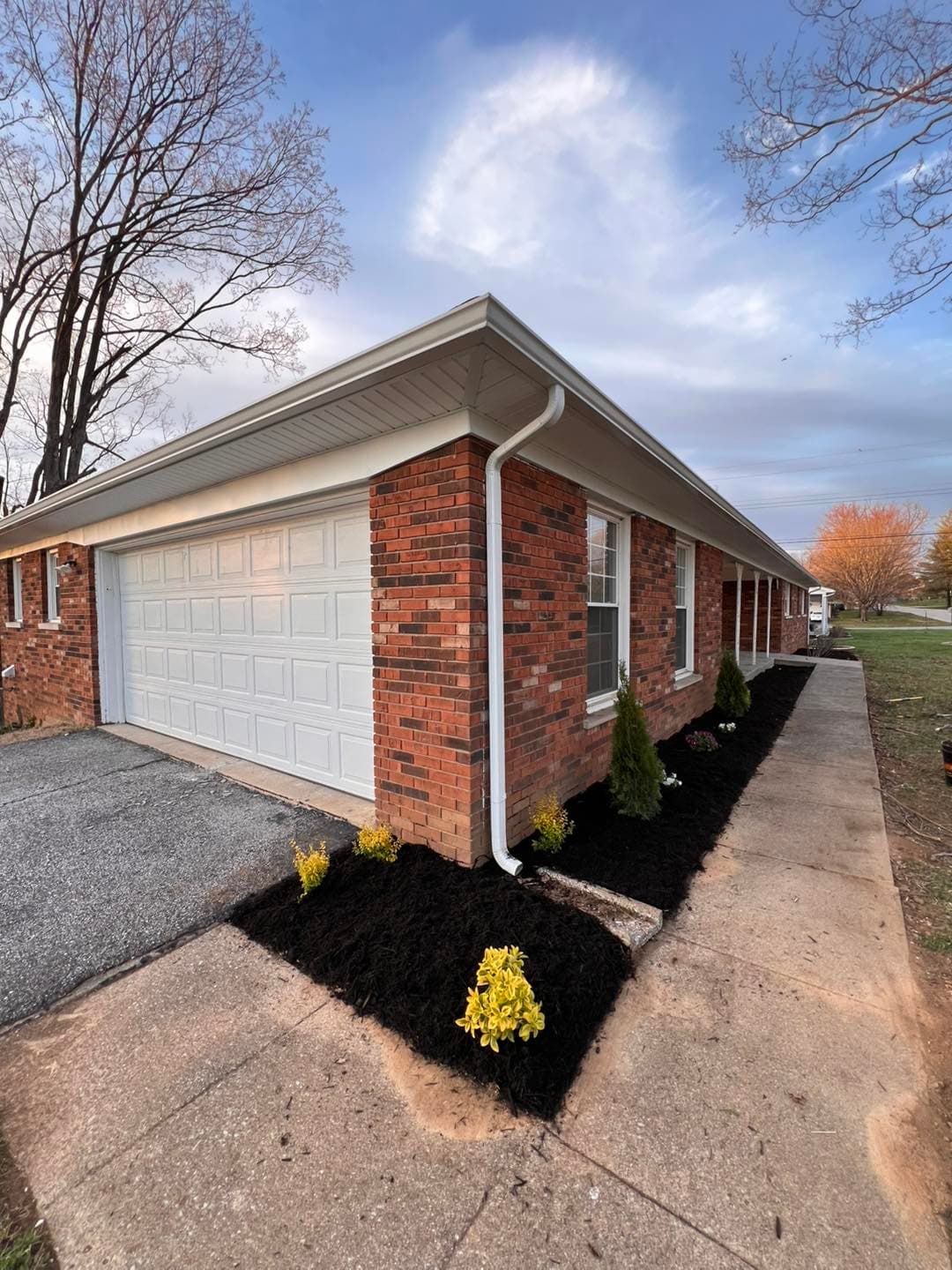 Brick house exterior with garage, fresh landscaping, and flowering plants in spring.