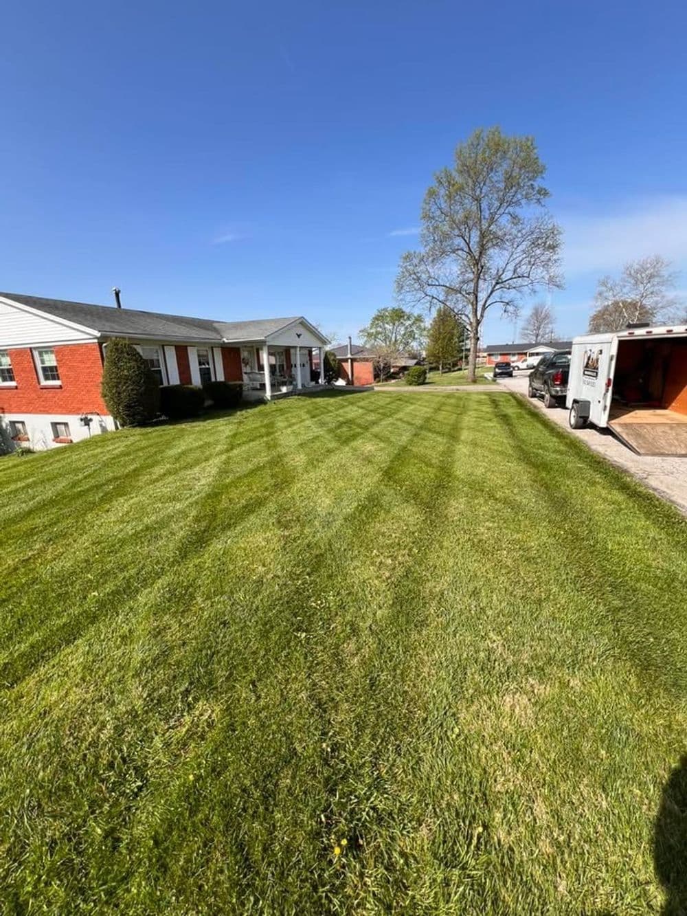Well-maintained lawn with striped pattern in front of a brick house under a clear blue sky.