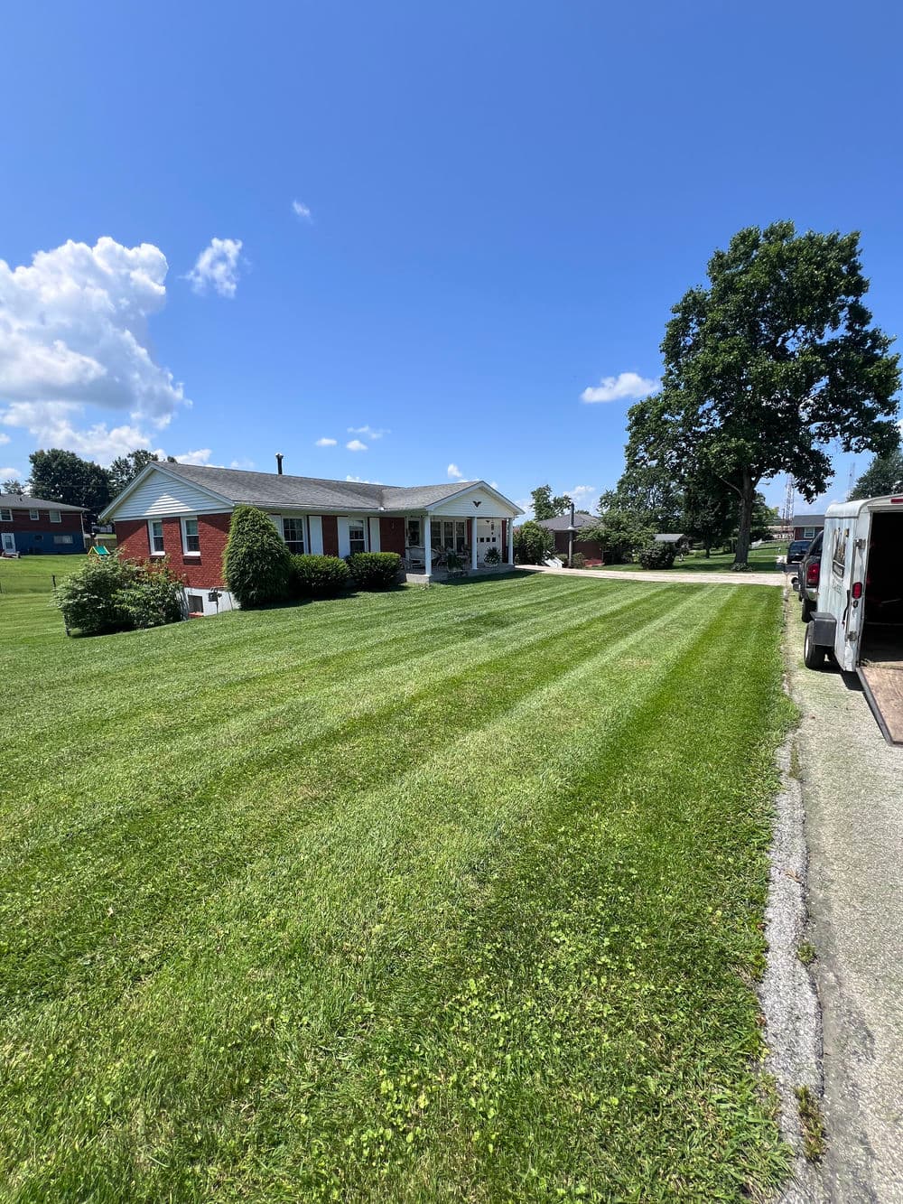 Lawn with freshly mowed grass in front of a residential brick house under a clear blue sky.