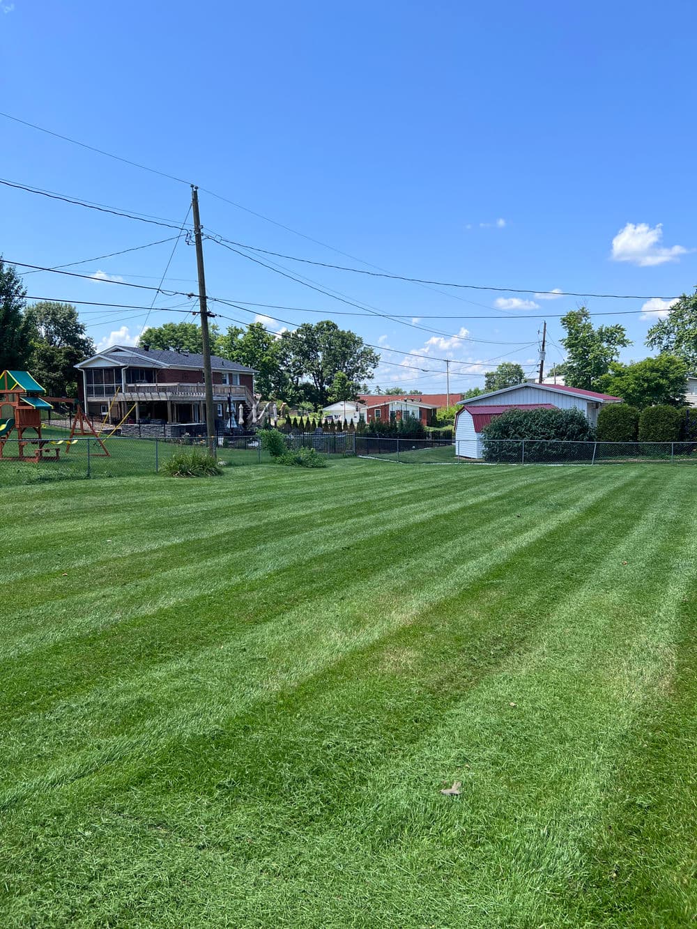 Lush green lawn with striped grass, playground equipment, and a house in the background.