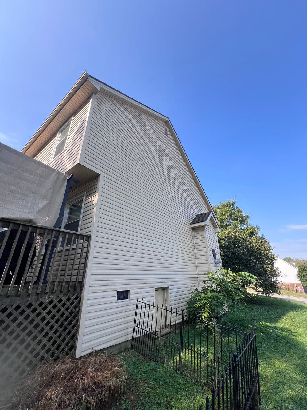 Side view of a light-colored house with a wooden deck and clear blue sky backdrop.