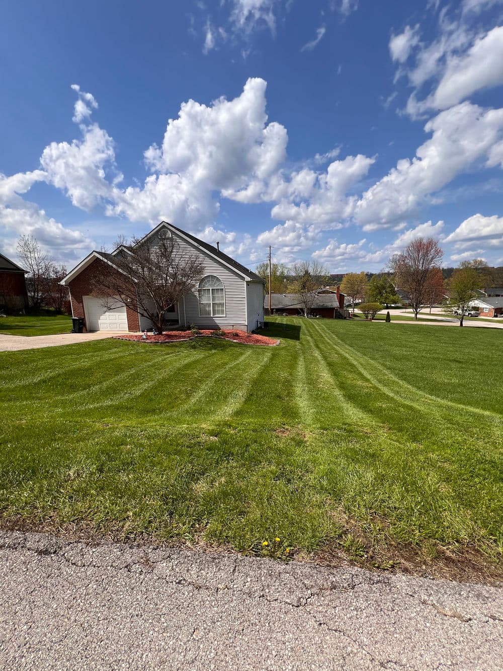 Single-story house with manicured lawn and cloudy blue sky in suburban neighborhood.