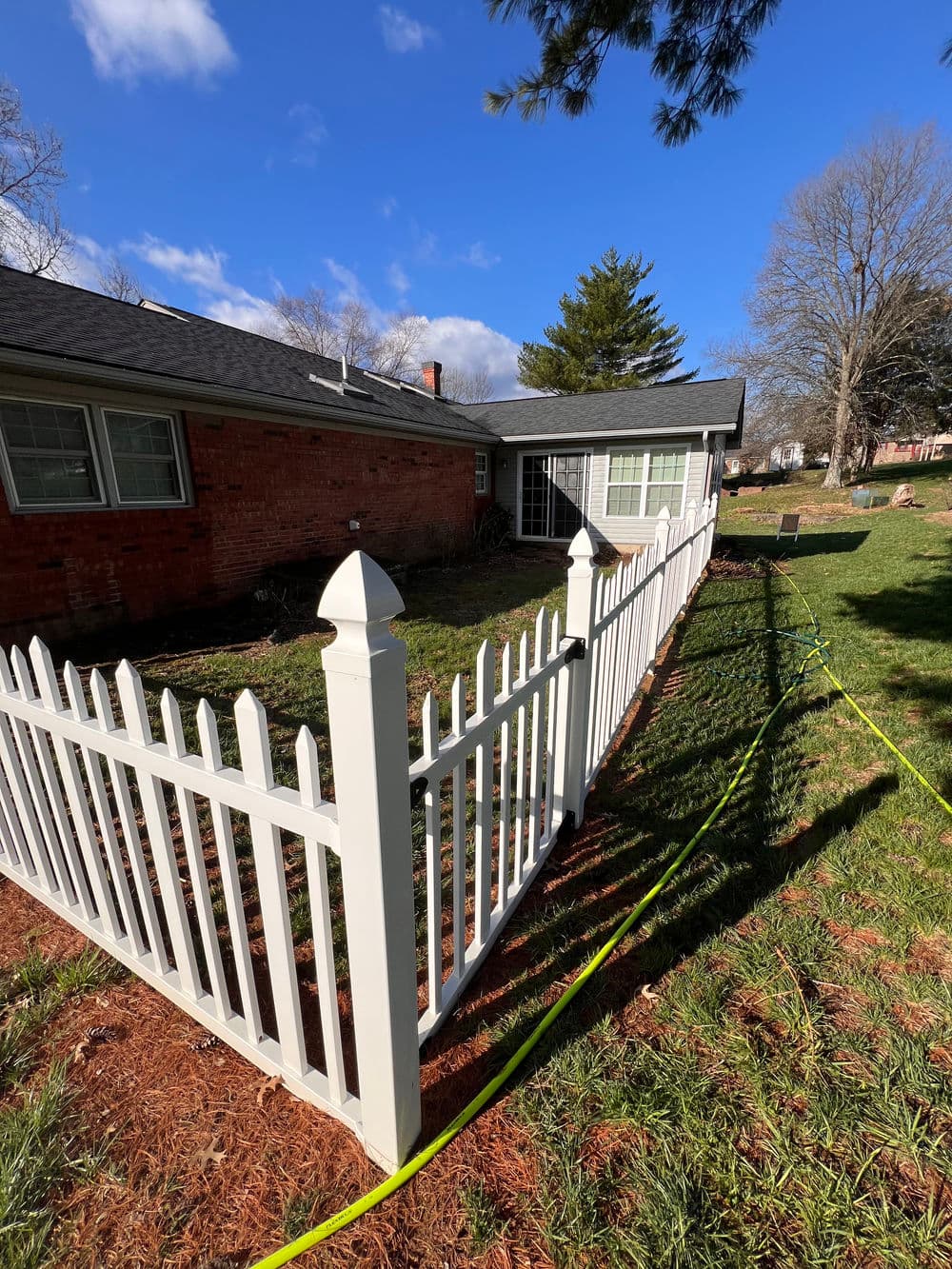 White picket fence surrounding a well-maintained yard with a blue sky and green grass.
