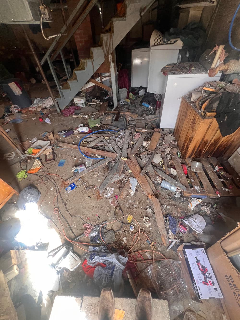 Cluttered basement with debris, furniture, and scattered items on the floor.