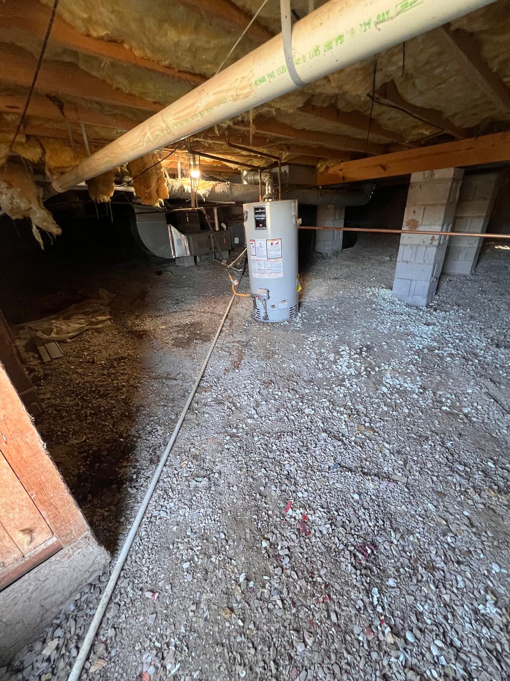 Crawl space showing water heater, ductwork, and gravel flooring under home.