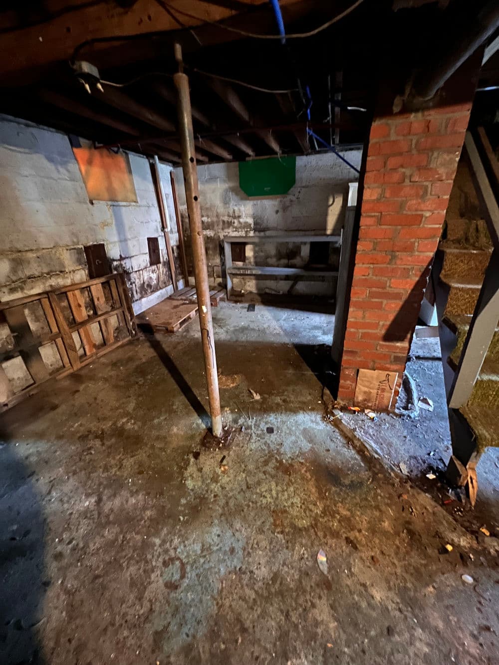 Clean, empty basement with concrete floor, exposed beams, and brick support column.
